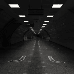 A picture of a road within a tunnel with symmetrical lighting on the top.