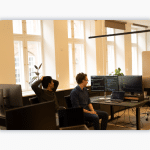 Two colleagues sit in front of a desktip setup with coding screens visible.