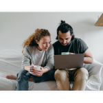 A couple sits on a couch and looks at their laptop