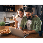 A couple is sitting in front of a laptop in their kitchen and is shopping online.