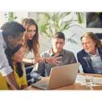 A group of colleagues sit together at a desk and discuss something they see on a laptop.